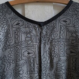 May include: A gray and black patterned dress with a black neckline and a button closure. The dress has a geometric pattern with a variety of shapes and designs.