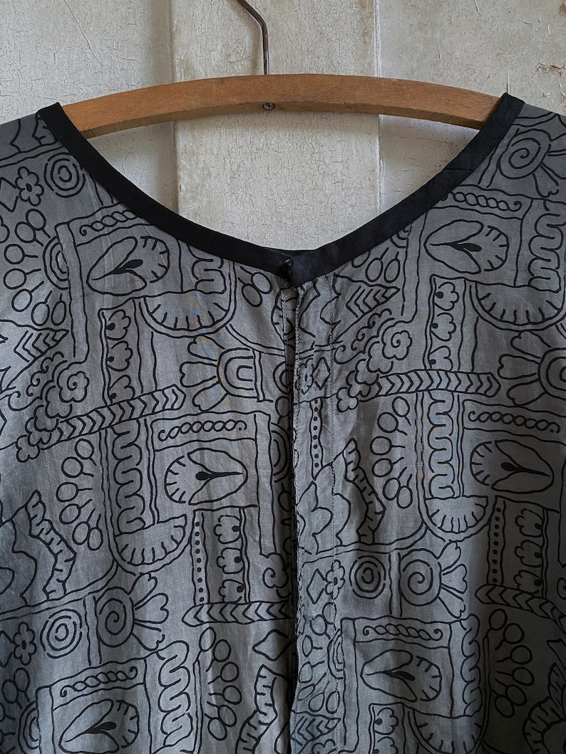 May include: A gray and black patterned dress with a black neckline and a button closure. The dress has a geometric pattern with a variety of shapes and designs.