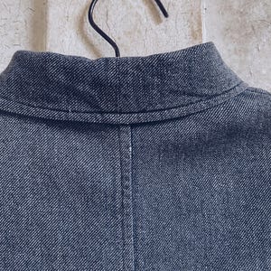 May include: Close-up of the collar of a dark blue denim jacket. The collar is folded down and has a single stitch running along the edge.