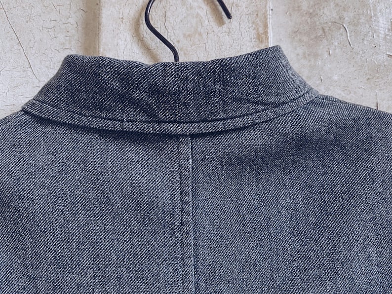 May include: Close-up of the collar of a dark blue denim jacket. The collar is folded down and has a single stitch running along the edge.