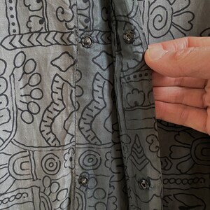 May include: A gray cotton shirt with a black and white geometric print. The shirt has a button-up front and a long sleeve.