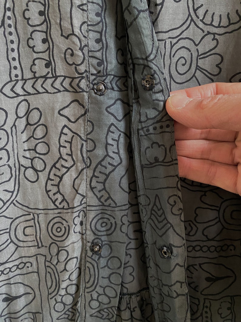 May include: A gray cotton shirt with a black and white geometric print. The shirt has a button-up front and a long sleeve.