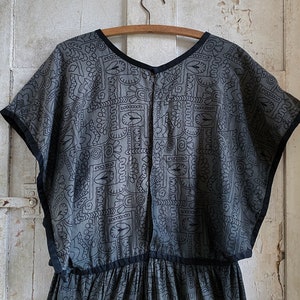 May include: A gray and black patterned dress with short sleeves and a gathered skirt. The dress has a black trim around the neckline and sleeves.