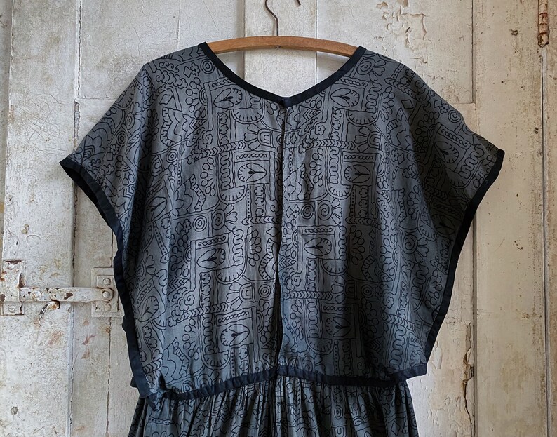 May include: A gray and black patterned dress with short sleeves and a gathered skirt. The dress has a black trim around the neckline and sleeves.