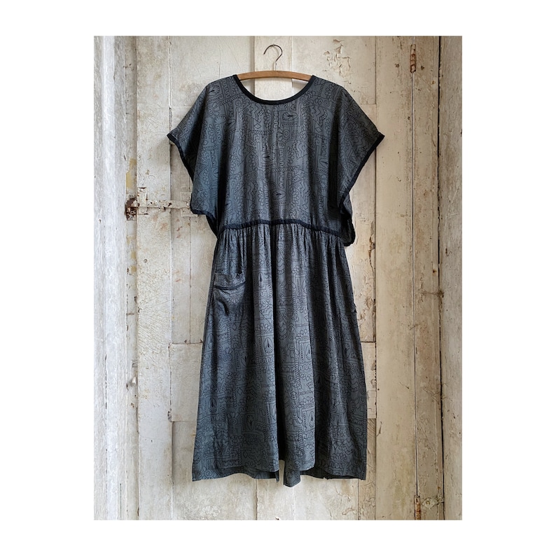 May include: A gray and black patterned dress with short sleeves and a gathered waist. The dress has a single pocket on the left side.