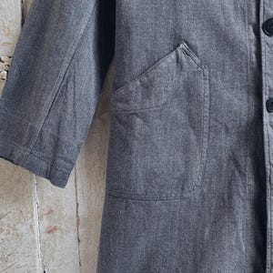 May include: A gray denim jacket with a large patch pocket on the front. The jacket has a button closure and two buttoned pockets on the front.