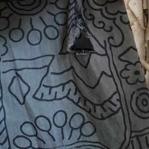 May include: A gray fabric with a black and white abstract pattern. The fabric has a tear in the upper right corner.