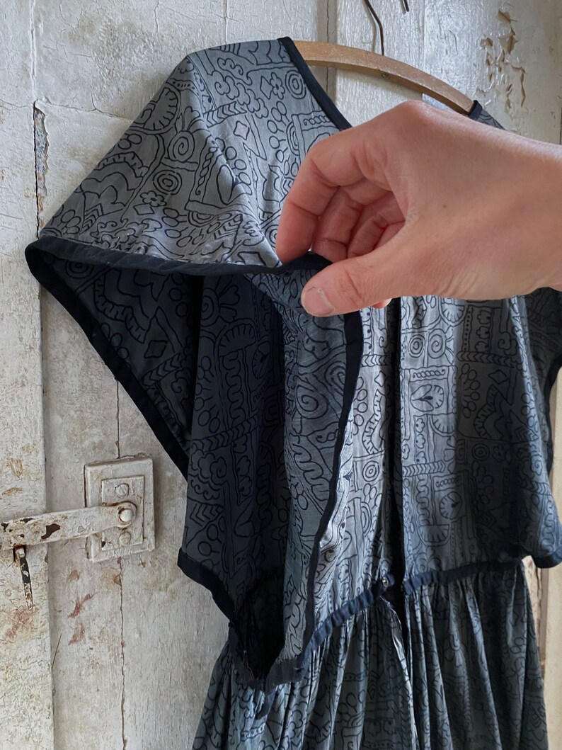 May include: A gray and black patterned dress with a gathered skirt and short sleeves. The dress has a black trim around the neckline and sleeves.