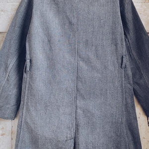 May include: A long, gray, denim jacket with a single-breasted closure and two pockets on the front. The jacket has a slightly textured surface and a relaxed fit.