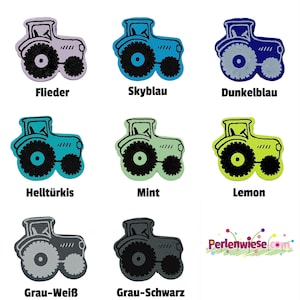 Könnte beinhalten: Eine Sammlung von acht traktorförmigen Knöpfen in verschiedenen Farben, darunter Flieder, Skyblau, Dunkelblau, Türkis, Mint, Lemon, Grau-Weiß und Grau-Schwarz. Jeder Knopf zeigt eine schwarze Traktorkontur und schwarze Räder.