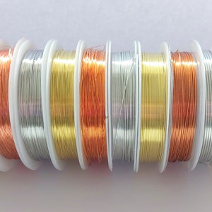 Könnte beinhalten: Ein Satz mit 10 Spulen Draht in verschiedenen Metallic-Farben, darunter Silber, Gold und Kupfer. Der Draht ist auf weißen Spulen aufgewickelt.