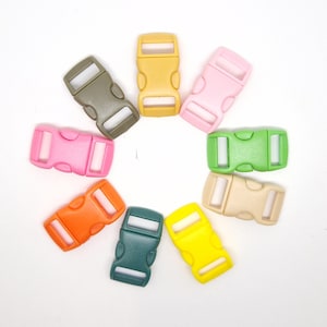 May include: A collection of colorful plastic side-release buckles in various shades, including pink, green, yellow, and orange. The buckles are arranged in a circular pattern against a white background. These are commonly used in crafting and DIY projects.