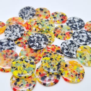 以下が含まれることがあります： カラフルな丸いボタンのコレクション。斑点模様のデザインです。ボタンは、黒、白、黄色、赤、オレンジなど、さまざまな色があります。各ボタンには、縫製用の穴が2つまたは4つあります。