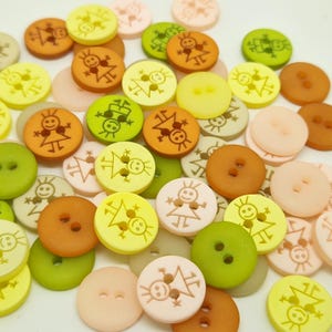 May include: A collection of round, two-hole buttons in shades of yellow, green, orange, and pale pink. Many of the buttons feature a printed line drawing of a smiling figure with spiky hair, while others are plain and solid in colour.