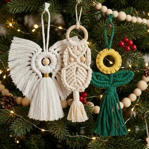 Puede incluir: Tres adornos de macramé colgados de un árbol. A la izquierda, un ángel blanco con cabeza de cuenta de madera. En el centro, un búho color crema con ojos de cuentas de madera. A la derecha, un adorno en forma de flor amarilla y verde.