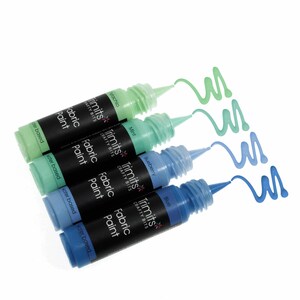 Może przedstawiać: Cztery butelki farby do tkanin w odcieniach niebieskiego i zielonego. Butelki są oznaczone "Trimits Crafty Bits Fabric Paint", a kolory to "Stachio", "Mint", "Blueberry" i "Blue".