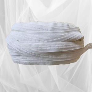 以下が含まれることがあります： テクスチャパターンが付いた白い伸縮性のあるトリム。トリムは折り畳んで巻かれています。