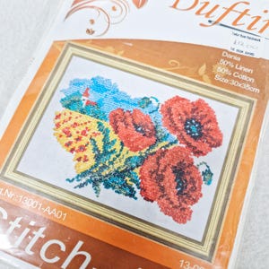 May include: A cross-stitch kit with a floral design, showcasing red poppies, yellow and blue details, and green leaves. The artwork is framed in a gold border. The kit contains 50% linen and 50% cotton, with dimensions of 30x35cm.