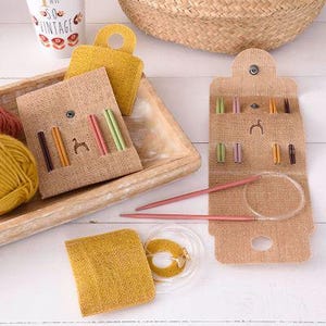 May include: A selection of knitting supplies, including a tan burlap needle case with colourful needles, a circular needle, and yellow yarn. The case has a button closure and a small horse silhouette.
