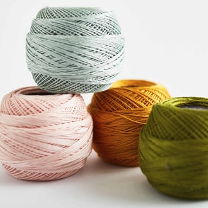 May include: Four balls of yarn in different colors: light blue, pink, orange, and green. The balls are stacked on top of each other.