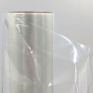 Może przedstawiać: Rolka przezroczystej, przezroczystej folii plastikowej. Rolka ma brązowy kartonowy rdzeń. Plastik jest częściowo rozwinięty, ukazując swoją błyszczącą, gładką powierzchnię. Tło jest jednolicie białe.