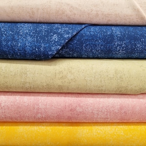 May include: A stack of fabric bolts in various colors. The colors include light beige, blue, light green, pink, and yellow. Each fabric has a speckled pattern. The blue fabric is folded over the top of the stack.