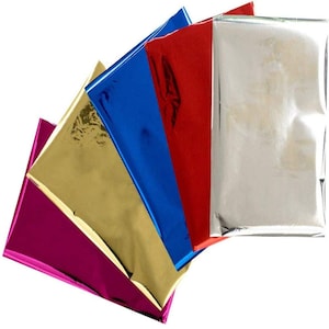 May include: A selection of shiny metallic sheets in gold, magenta, blue, red, and silver. The sheets have a reflective surface. The edges are neatly aligned, creating a visually appealing fan-like arrangement.