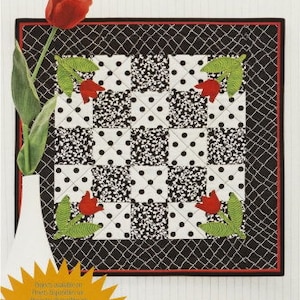 May include: A quilting template for making tulip designs. The template is 10.16 cm by 15.24 cm and is made of white fabric with black polka dots. The template is surrounded by a black border with a red and white checkered pattern. The text "TULIP TEMPLATE" is printed in black on a white background.