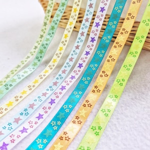May include: A selection of patterned ribbons in various colours. The ribbons display a repeating star design. Colours include light green, yellow, white, purple, and turquoise. The ribbons are suitable for crafts and gift wrapping.