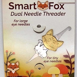 May include: A Smart Fox dual needle threader package. The packaging features a gold-coloured fox-shaped needle threader, designed for both large and tiny eye needles. The packaging has a nature-themed illustration with a fox and mushrooms.