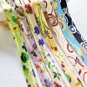 May include: A selection of patterned ribbons, showcasing floral and abstract designs. The ribbons display a variety of colours, such as green, purple, orange, and blue, with detailed botanical patterns and swirling geometric shapes. Suitable for crafts and gift wrapping.