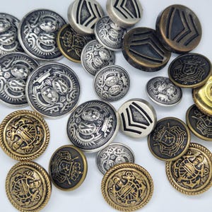 May include: Assortment of metal buttons in various designs. Some buttons are silver with intricate patterns, while others are gold with a more ornate design. There are also buttons with a simple chevron pattern.