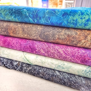 Könnte beinhalten: Ein Stapel aus fünf Stoffquadraten mit verschiedenen Marmormustern. Das oberste Quadrat ist blau und grün, das zweite ist braun und grau, das dritte ist lila, das vierte ist weiß mit grünen Akzenten und das unterste Quadrat ist grau.