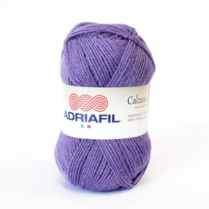 Könnte beinhalten: Eine violette Garnrolle mit der Aufschrift "Calzaso" und der Marke "ADRIAFIL". Der Text "superwash virgin laine vierge superfine" ist ebenfalls sichtbar.
