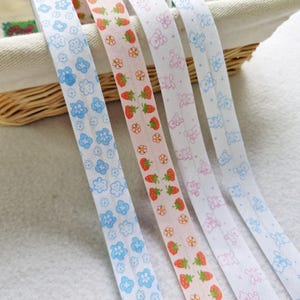 May include: Five decorative ribbons with repeating patterns. Designs include blue flowers, strawberries, pink teddy bears, and blue teddy bears. The ribbons are white and pastel colors, perfect for crafts and gift wrapping.