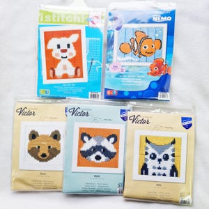 May include: Five different craft kits for needlepoint embroidery. The kits feature various animal designs, including a white lamb, a clownfish, a fox, a raccoon, and an owl. The kits are packaged in clear plastic bags with colourful designs and instructions.