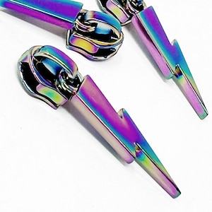 May include: Iridescent lightning bolt zipper pulls. The metal zipper pulls have a rainbow finish with shades of purple, blue, green, and yellow. The zipper pulls are on a white background.