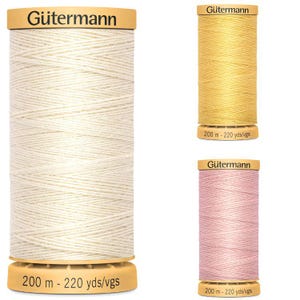 May include: Three spools of Gütermann thread in cream, yellow, and pink. Each spool has a tan base and top with the Gütermann logo. The cream spool is the largest, with the text "200 m - 220 yds/vgs" on the base.