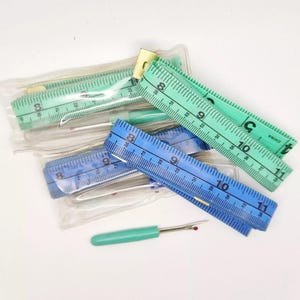 May include: A set of three measuring tapes in blue and green, with a small green seam ripper. The tapes are marked in inches and are packaged in clear plastic.