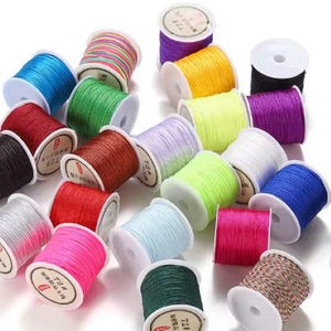 May include: A collection of colorful spools of thread in various shades, including blue, green, red, pink, and yellow. The spools are arranged on a white surface, showcasing the vibrant colors and textures of the thread.