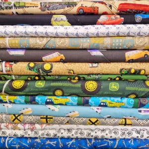 May include: A stack of folded fabric bolts featuring various patterns including trains, vintage cars, sailboats, grid lines, camper vans, tractors, John Deere logos, construction trucks, railroad crossing signs, bicycles, and metal wrenches on colourful backgrounds.