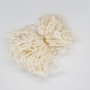 May include: A fluffy white yarn ball with a gold ribbon tied around it.