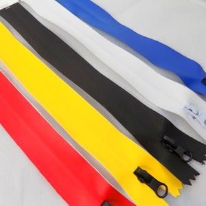 Puede incluir: Cinco cintas de cremallera de diferentes colores, incluyendo rojo, amarillo, negro, blanco y azul. Las cremalleras están dispuestas en una fila, con la cremallera roja en la parte inferior y la cremallera azul en la parte superior.