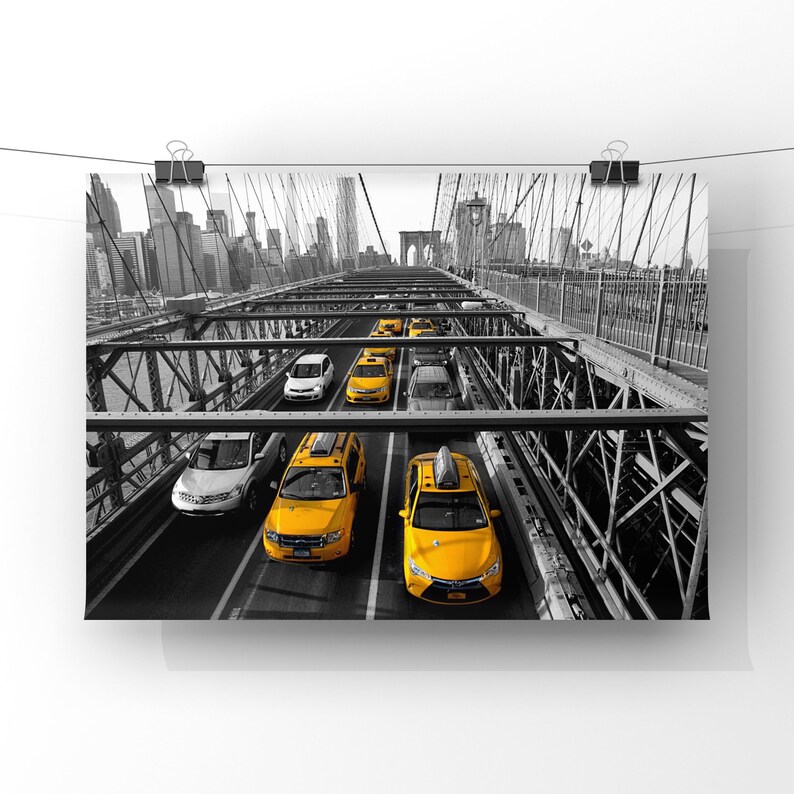 May include: A black and white photo of yellow taxis driving across the Brooklyn Bridge in New York City.