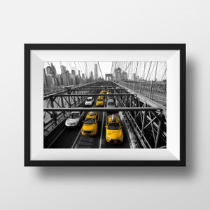 May include: A black and white photo of yellow taxis driving across the Brooklyn Bridge in New York City. The bridge is made of steel and has a lot of cables. The city skyline is visible in the background.