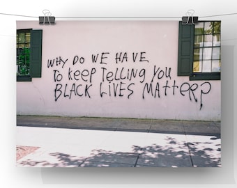 Può includere: Un muro di mattoni bianchi con vernice spray nera che recita "WHY DO WE HAVE TO KEEP TELLING YOU BLACK LIVES MATTER?" Il muro ha due finestre in legno verde con cornici bianche.