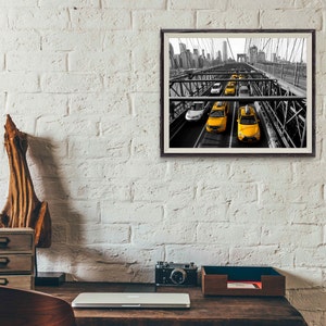 May include: Black and white photograph of yellow taxis driving across a bridge in New York City. The bridge is a steel structure with a view of the city skyline in the background.
