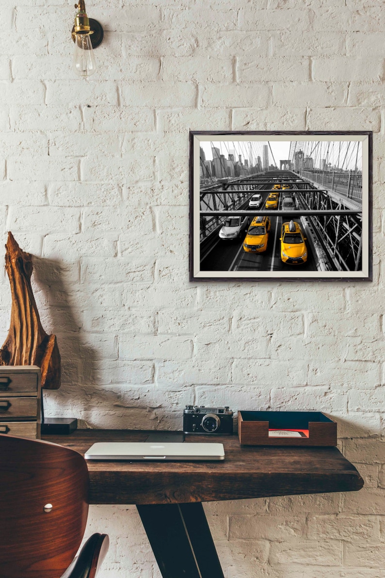 May include: Black and white photograph of yellow taxis driving across a bridge in New York City. The bridge is a steel structure with a view of the city skyline in the background.