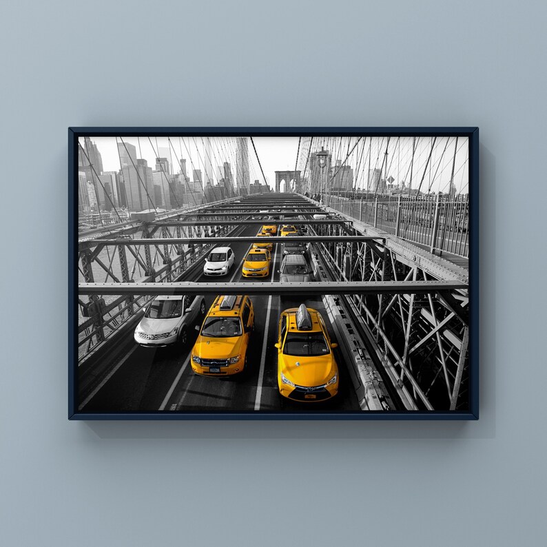 May include: A black and white photo of yellow taxis driving across the Brooklyn Bridge in New York City. The bridge is made of steel and has a lot of intricate details. The taxis are all facing the same direction and are driving in a line.