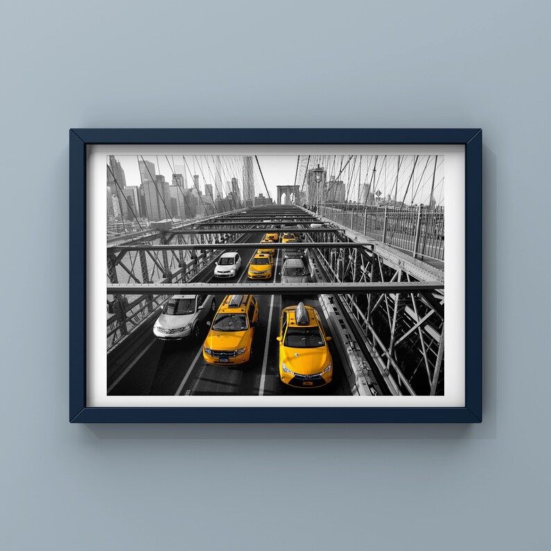 May include: A black and white photo of yellow taxis driving across a bridge in New York City. The bridge is made of metal and has a lot of support beams. The taxis are all in a line and are driving in the same direction. The city skyline is visible in the background.